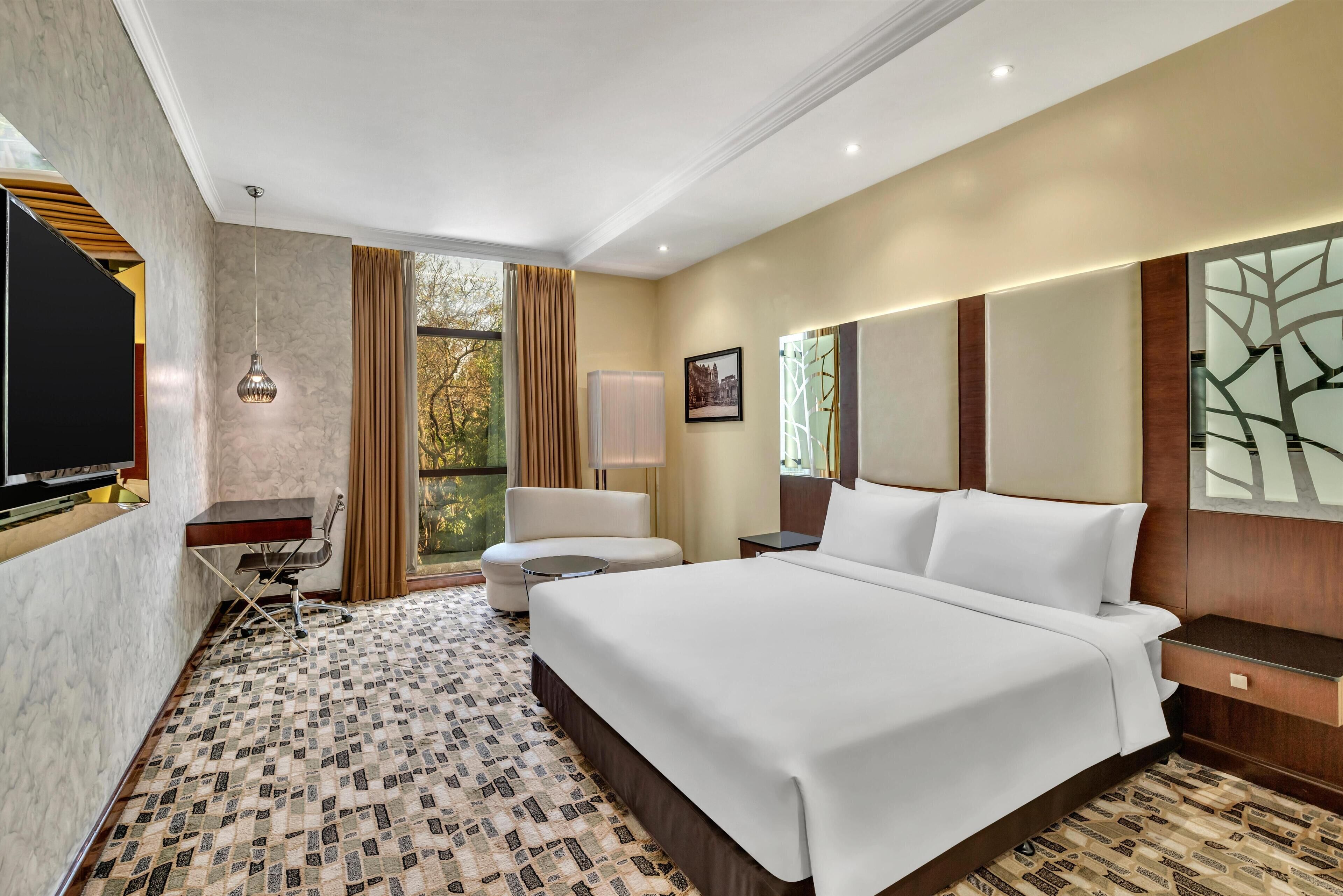 A hotel room with a large bed, a desk with a chair, a TV, and a window with curtains.