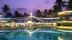 Zona de piscina con vista despejada al agua, rodeada de palmeras y luces colgantes.