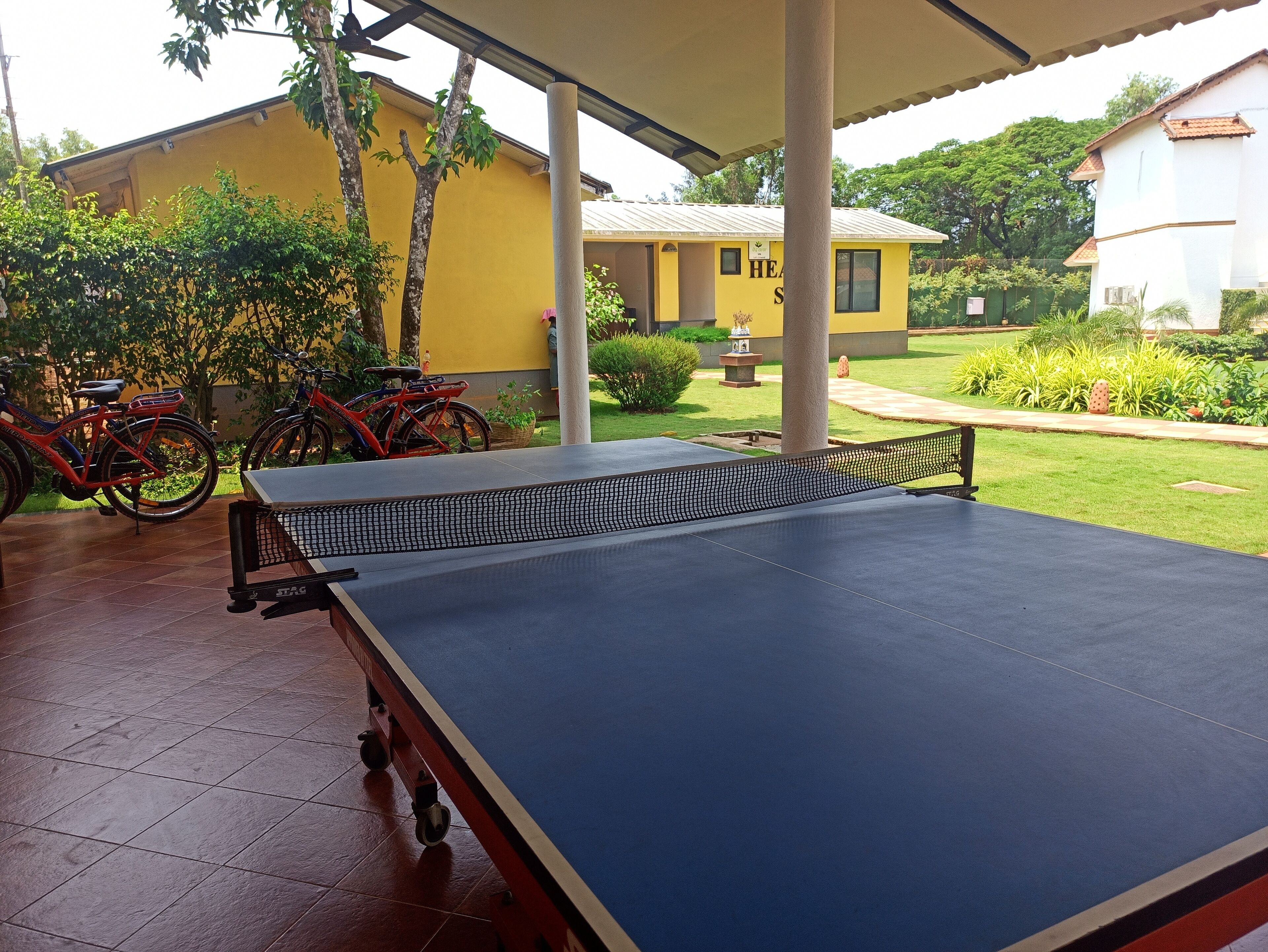 Una mesa de ping pong bajo una zona techada, con bicicletas estacionadas cerca.