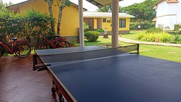 Una mesa de ping pong bajo una zona techada, con bicicletas estacionadas cerca.