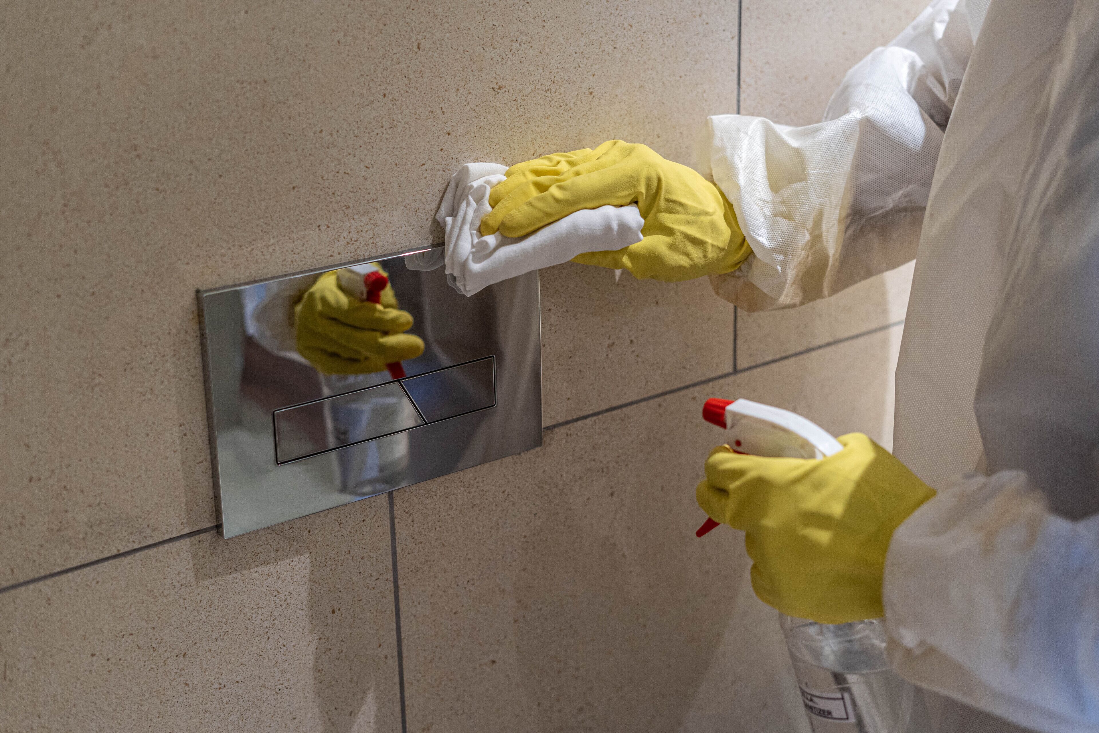 Una persona limpia una pared de azulejos con un pulverizador y un paño.