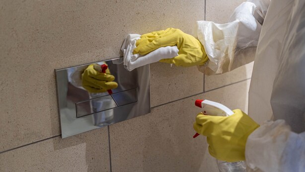 Iemand maakt een betegelde muur schoon met een sprayfles en doek.