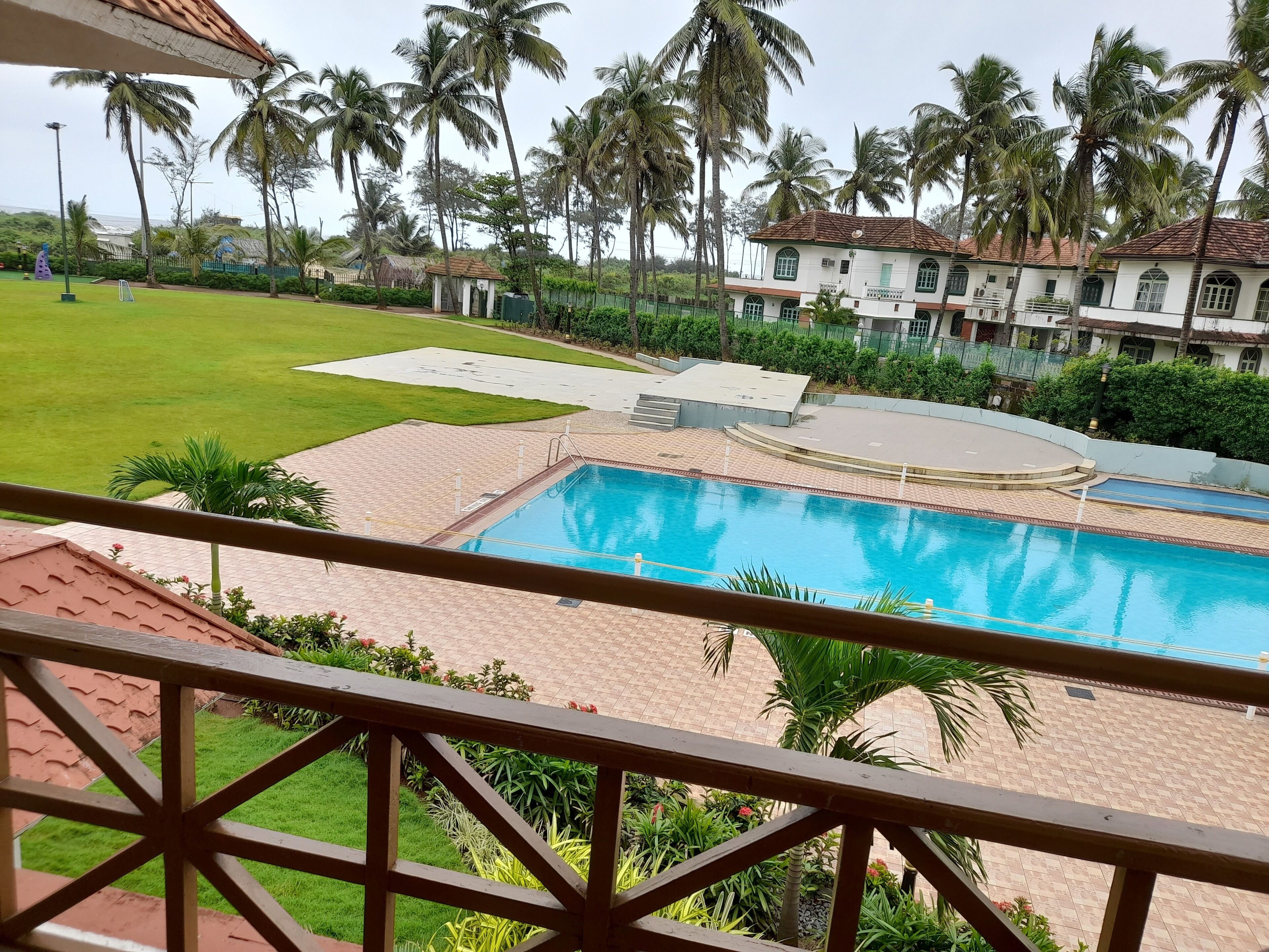 A swimming pool with a tiled deck, surrounded by palm trees and a well-maintained lawn.
