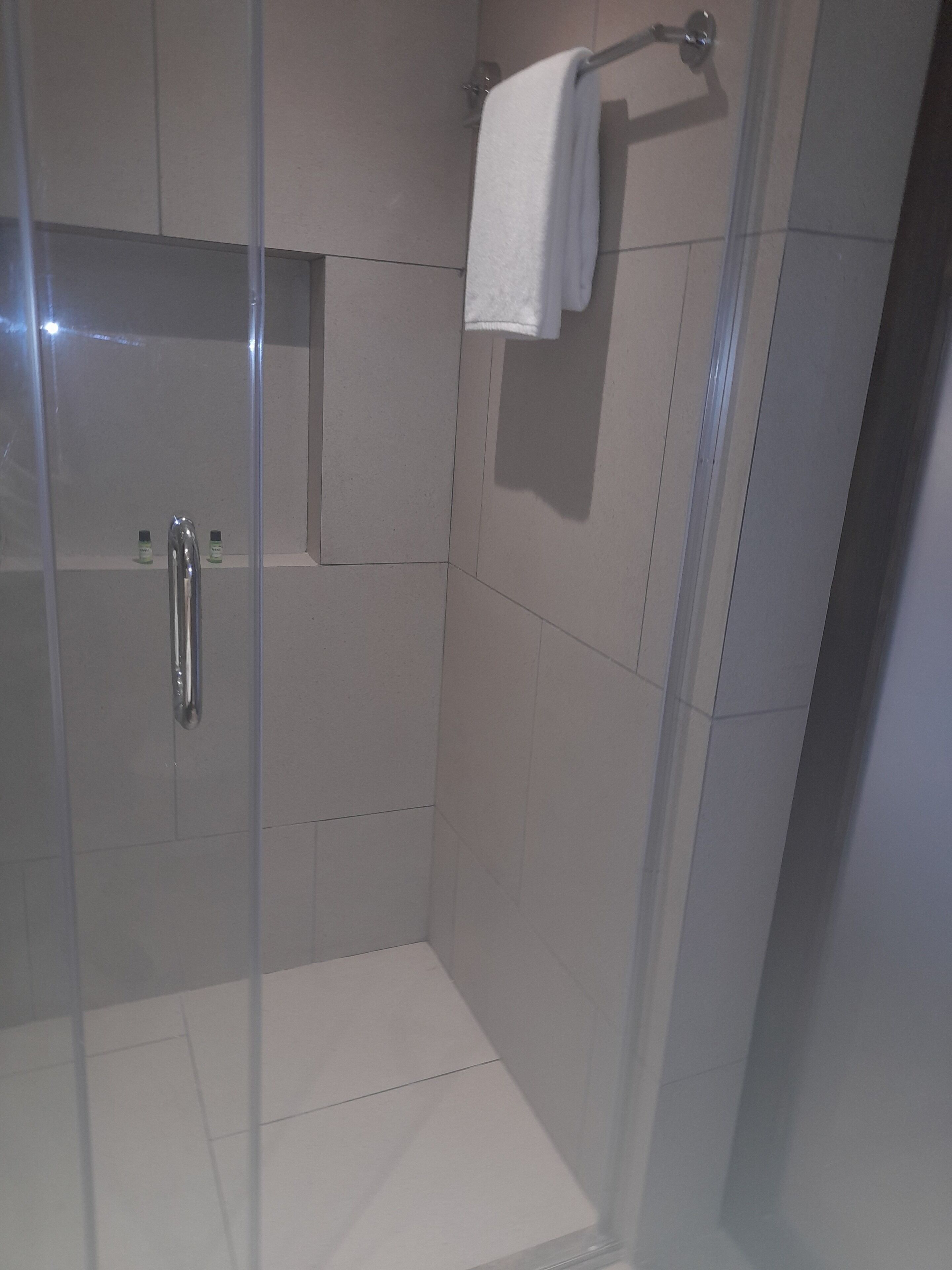 A modern shower stall with a glass door, a towel rack, and a shower control panel.