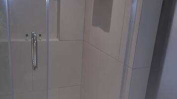 A modern shower stall with a glass door, a towel rack, and a shower control panel.