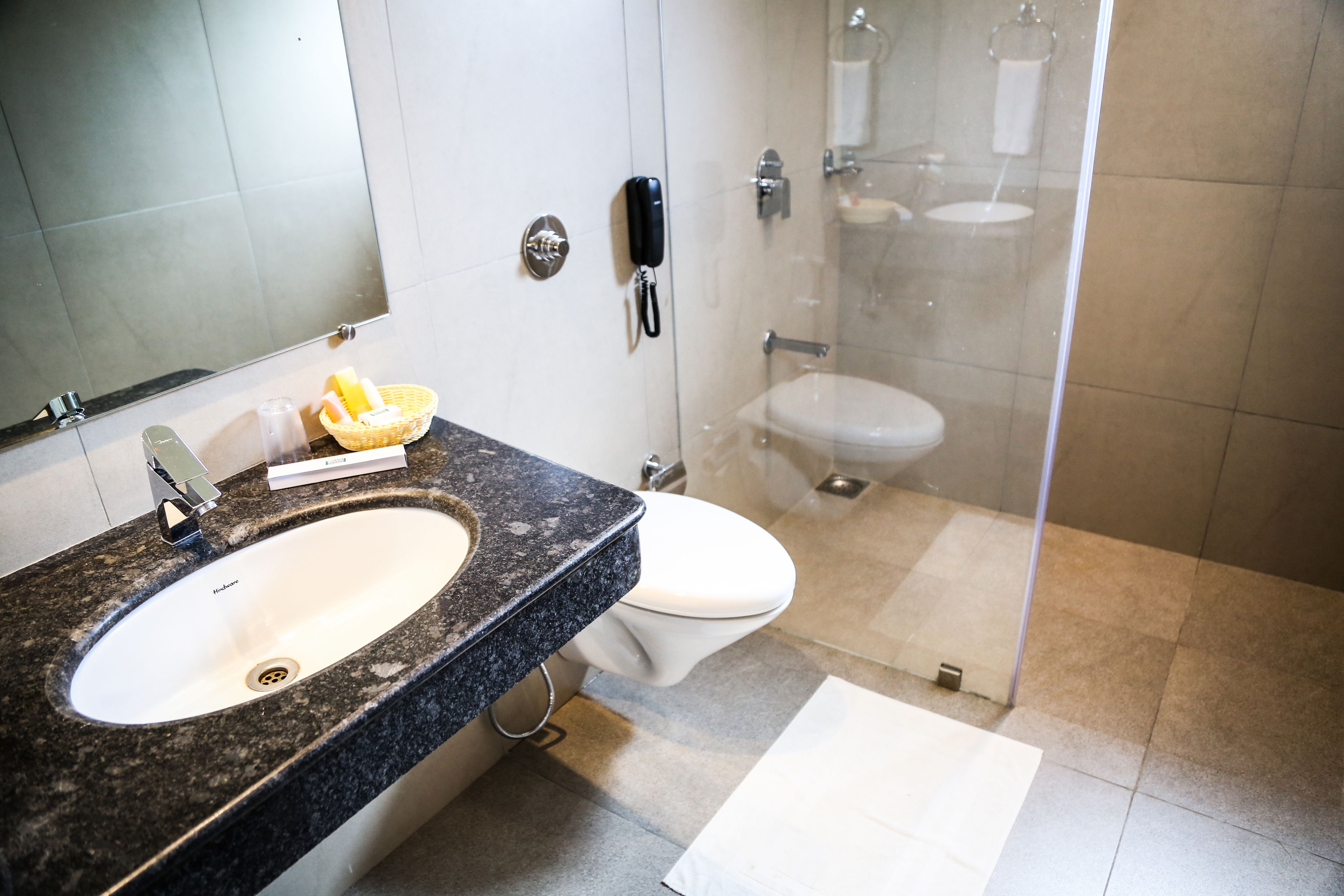 Un baño moderno con lavamanos de granito, un teléfono móvil, un inodoro y una zona de ducha con mampara de vidrio.