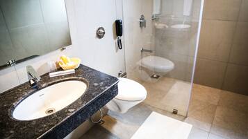 Un baño moderno con lavamanos de granito, un teléfono móvil, un inodoro y una zona de ducha con mampara de vidrio.
