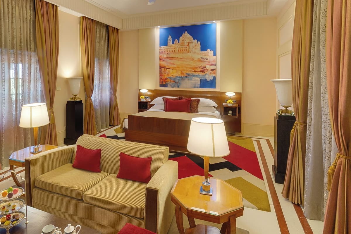 A hotel room with a bed, a sofa, a table, and a painting on the wall.