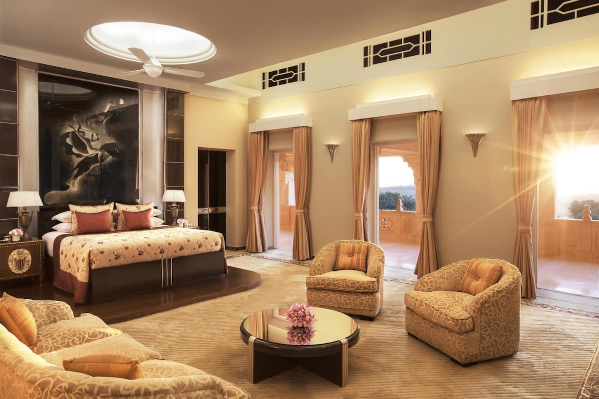 A spacious hotel room with a large bed, two armchairs, a coffee table, and a ceiling fan.