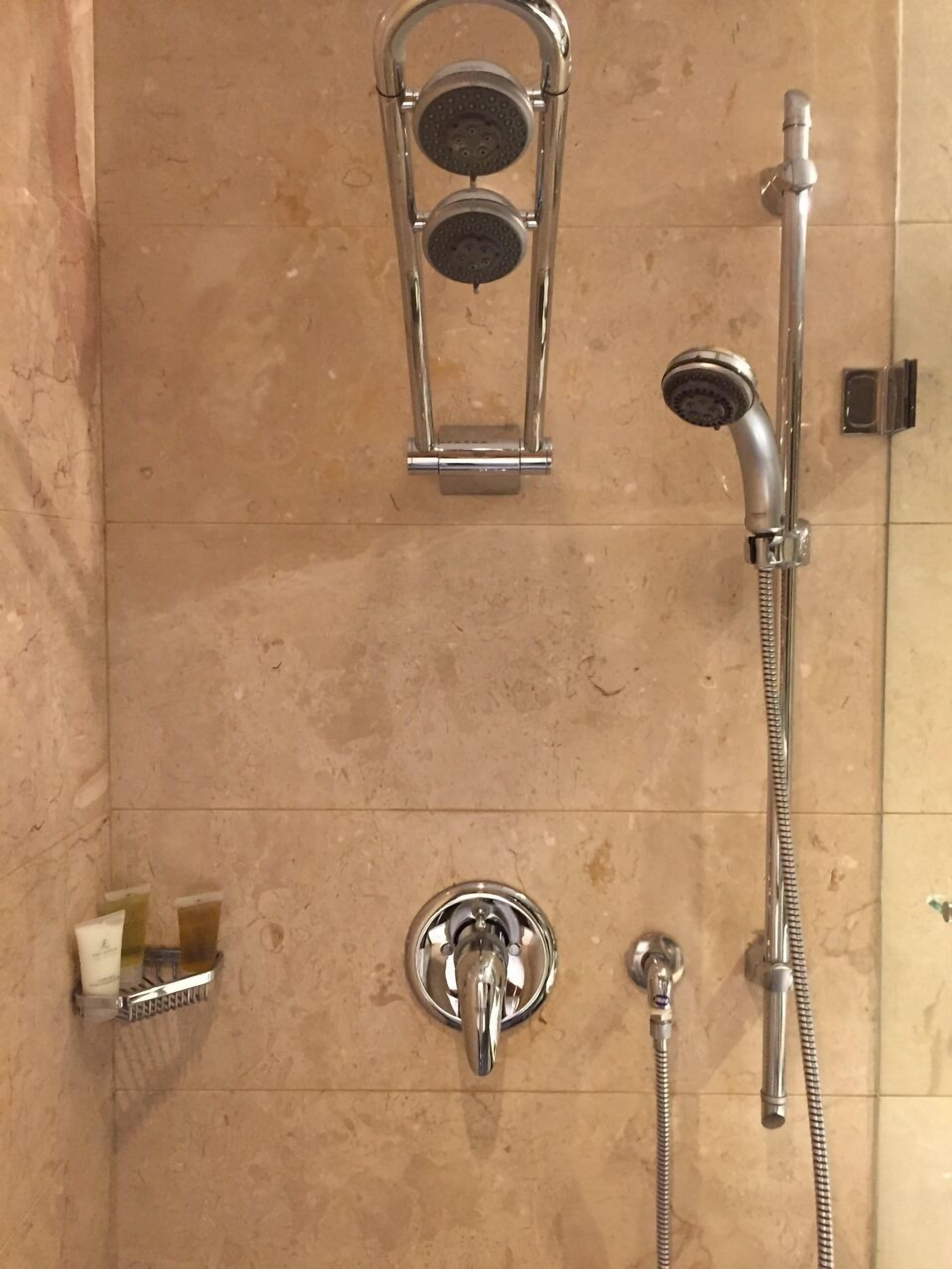 A bathroom with a shower, a handheld showerhead, and a wall-mounted faucet.