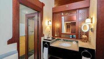 Un baño con puerta de madera, un lavabo con espejo y dos luces fijadas a la pared.