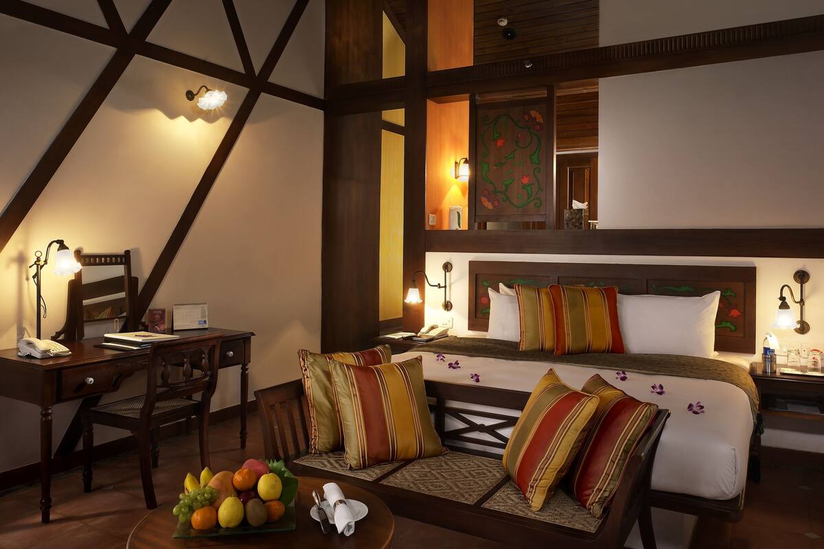 A hotel room with a bed, a desk, a chair, and a dining table with fruit.