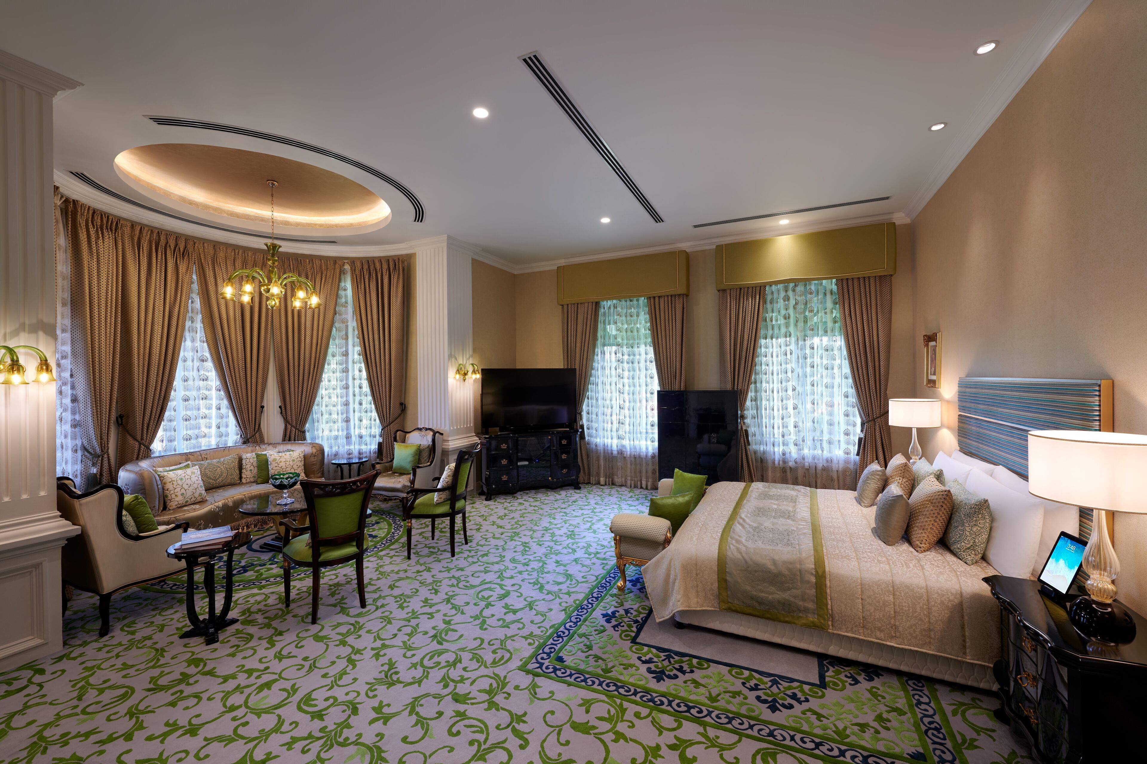 A spacious hotel room with a large bed, a sofa, a TV, and a dining area.