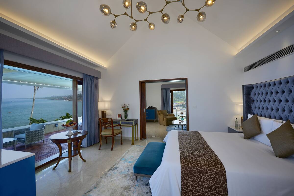 A modern hotel room with a large bed, a desk, and a view of the sea.