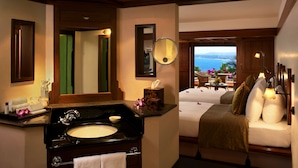 A hotel room with a wooden ceiling, a large window with a view of the sea, a bed with white bedding, and a bathroom with a sink and mirror. - The Leela Kovalam, a Raviz Hotel (Neyyattinkara)