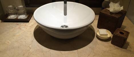 A bathroom sink with a white basin, two faucets, and a mirror above. There are two glass jars on a tray, a tissue box, and a soap dish on the counter.