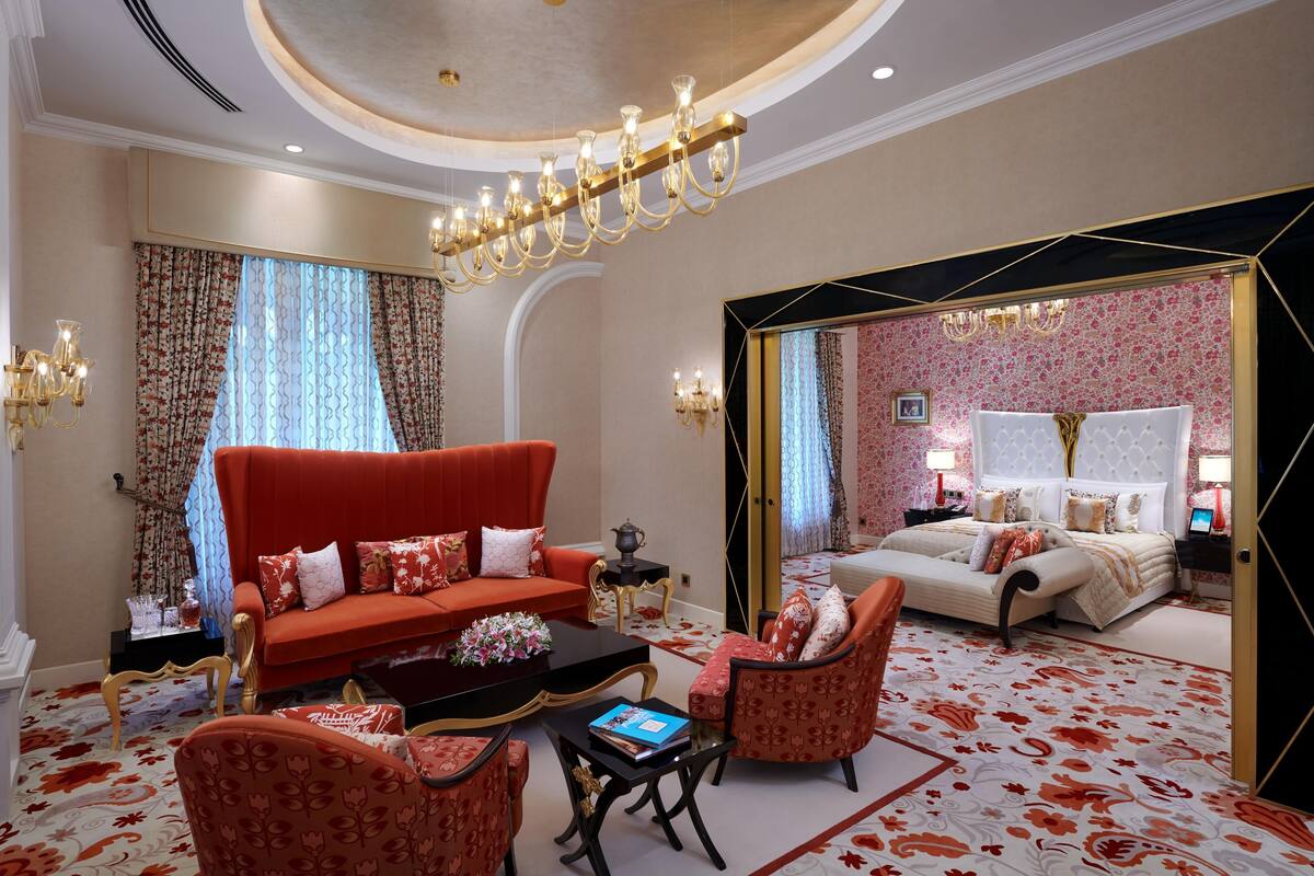 A hotel room with a red sofa, matching armchairs, a coffee table, and a bed with a white headboard.