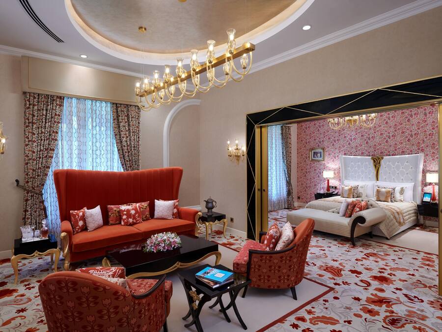 Une chambre d’hôtel avec un canapé rouge, des fauteuils assortis, une table basse et un lit doté d’une tête de lit blanche.