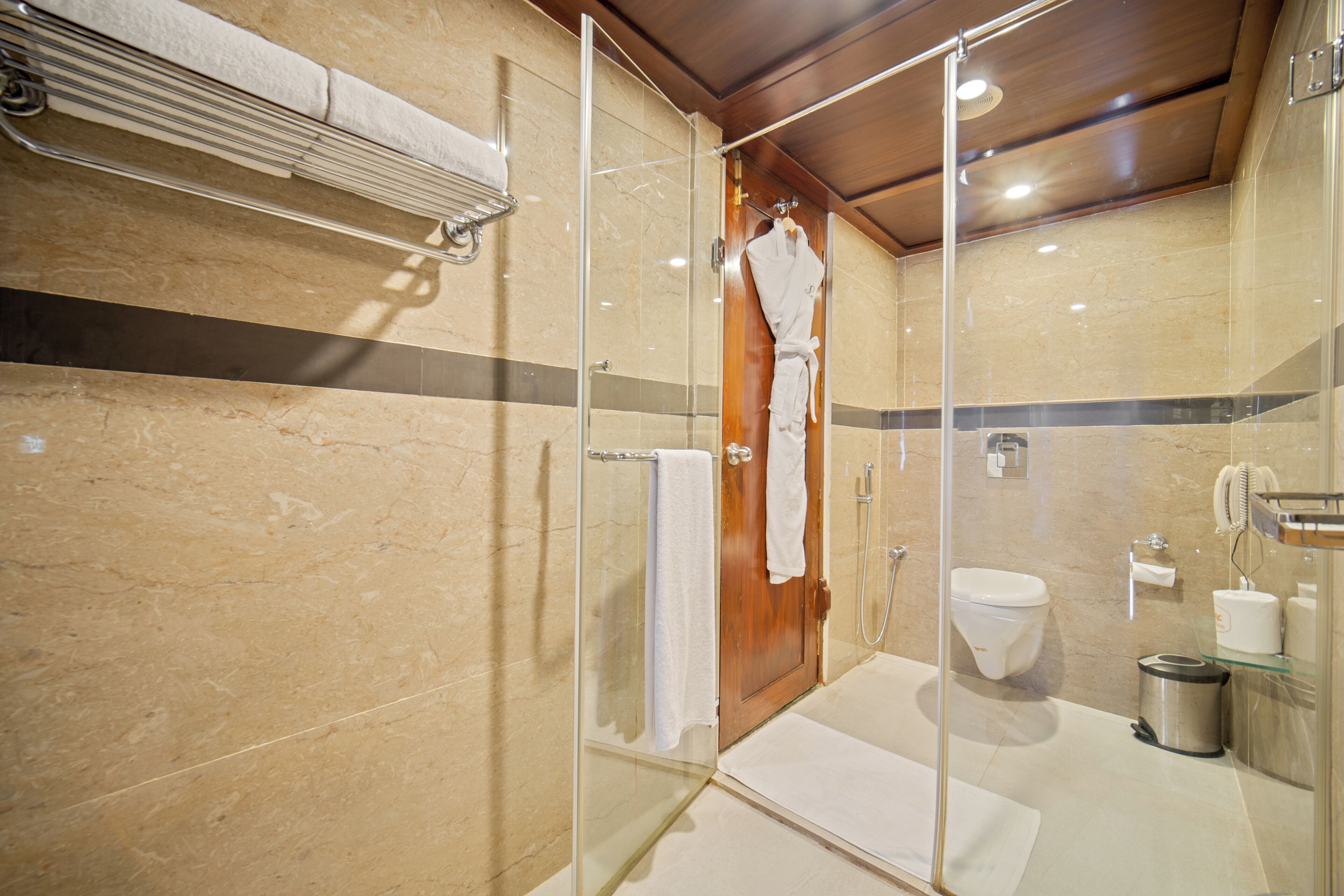Un bagno moderno con cabina doccia in vetro, porta in legno, un water e un lavandino.
