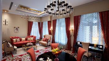 A spacious living room with a chandelier, red and white patterned curtains, a dining table with fruit, and a sofa set.