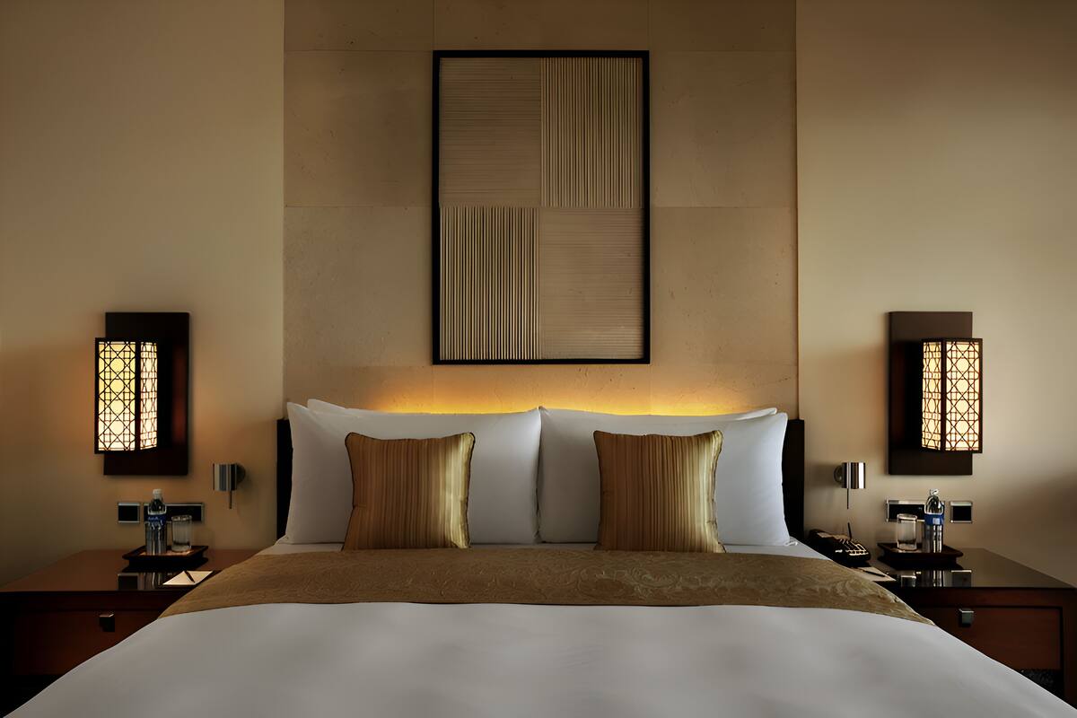 A hotel room with a large bed, two bedside tables, a wall-mounted artwork, and two wall sconces.