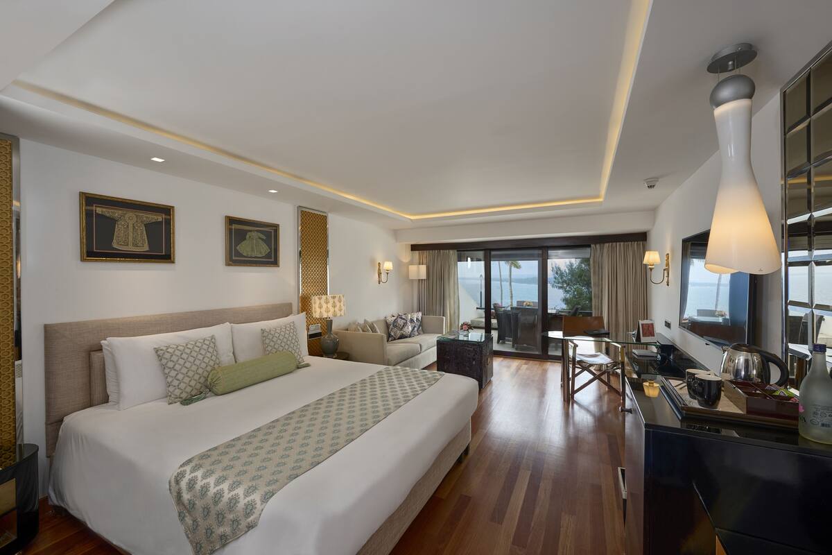 A spacious hotel room with a large bed, a dining area, and a view of the sea.