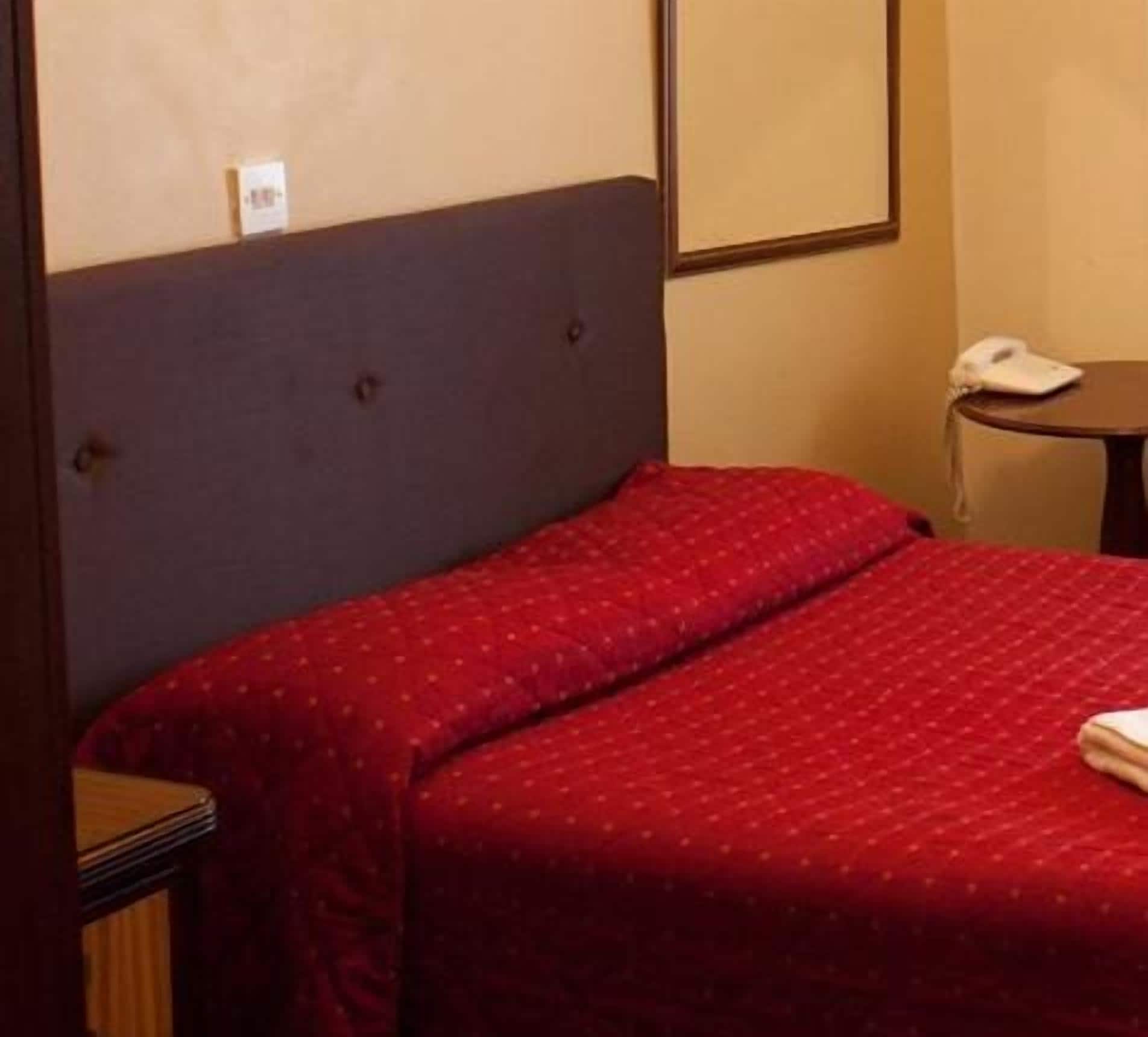 A hotel room with a single bed, a bedside table with a phone, and a small round table.