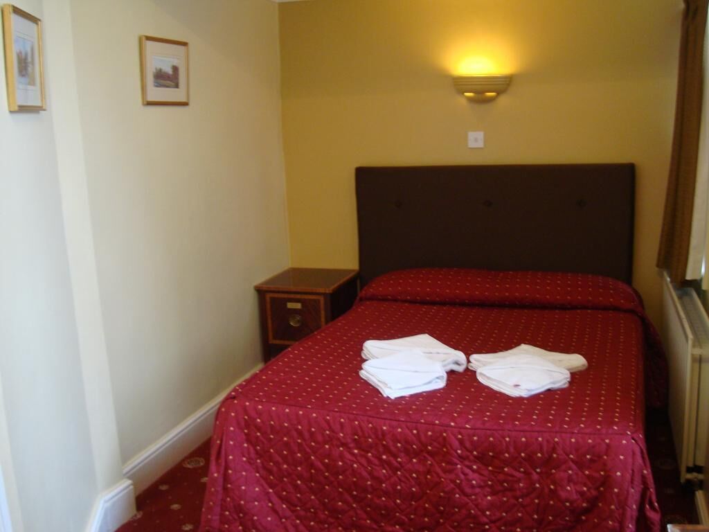 A hotel room with a double bed, a nightstand, and a wall-mounted light fixture.