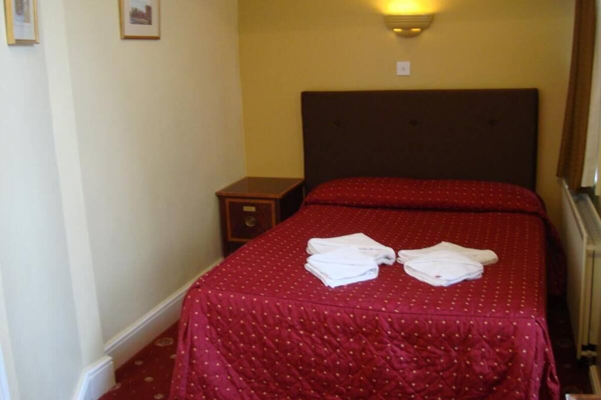 A hotel room with a double bed, a nightstand, and a wall-mounted light fixture.