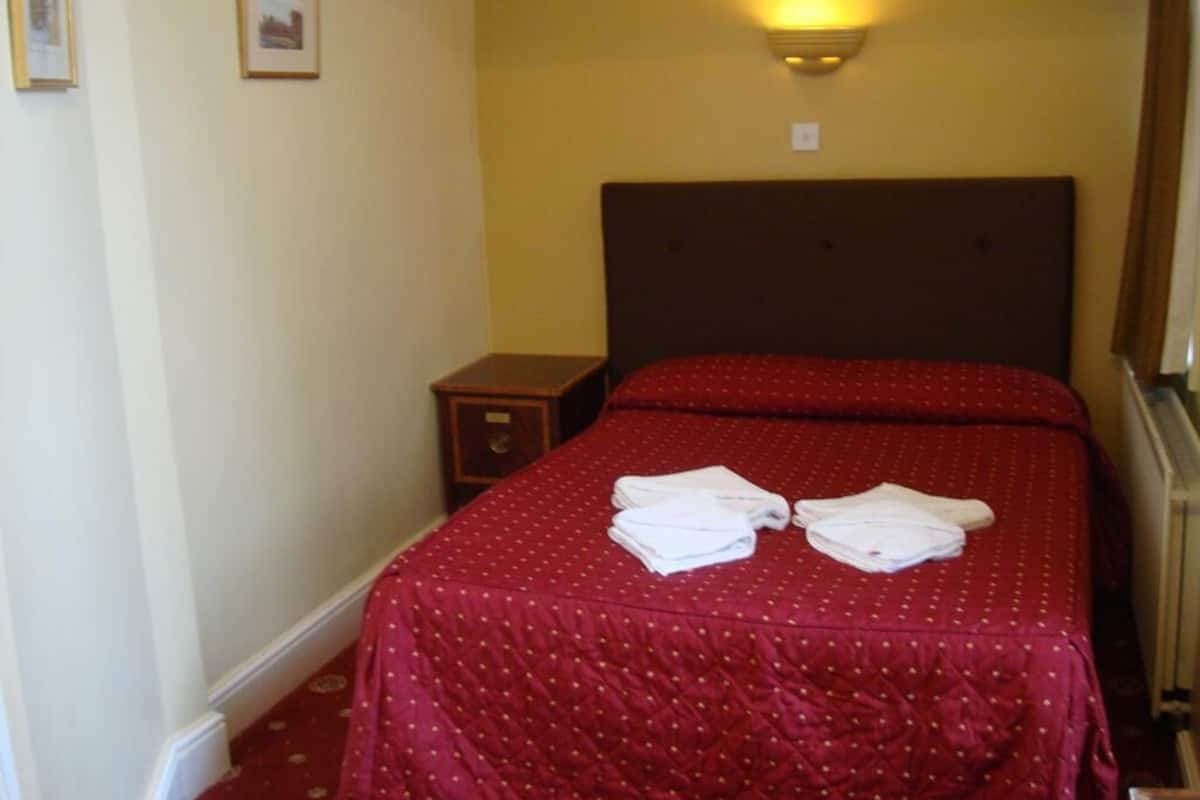 A hotel room with a double bed, a nightstand, and a wall-mounted light fixture.