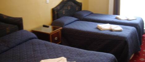 Een hotelkamer met drie bedden, elk voorzien van een donkerblauwe plaid en keurig opgevouwen handdoeken.