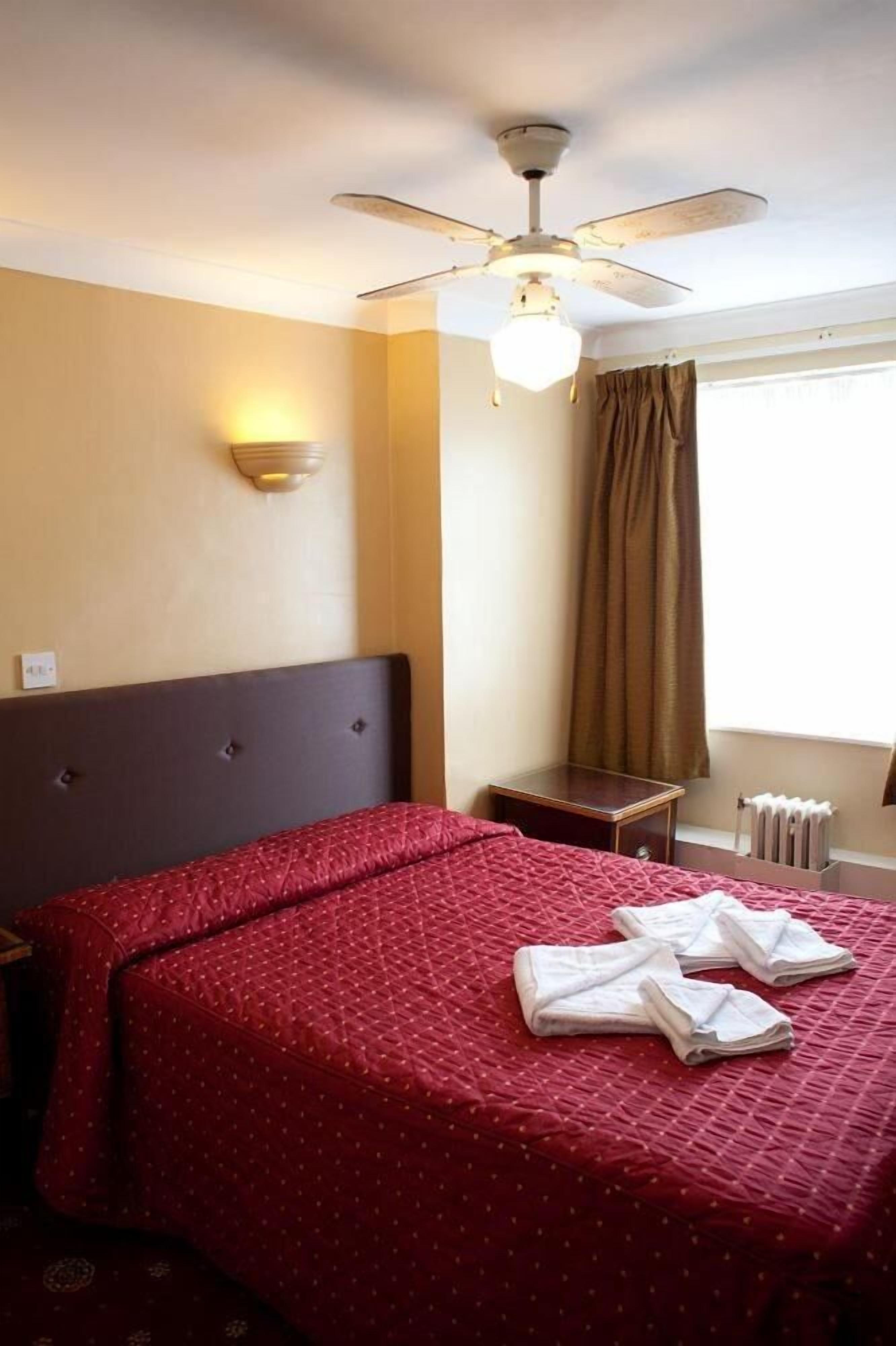 A hotel room with a bed, a ceiling fan, a nightstand, and a window with curtains.
