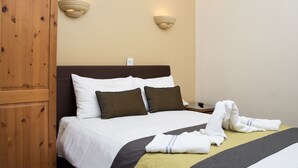 A neatly made bed with white and striped pillows, a brown headboard, and a wooden wardrobe. - Rose Court Hotel (London)