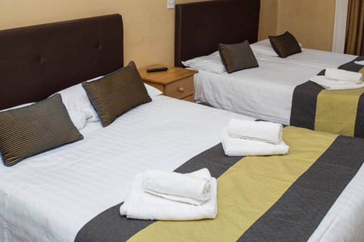 A hotel room with two beds, each with white linens and brown headboards. There are folded towels on the beds and a wooden nightstand between them.