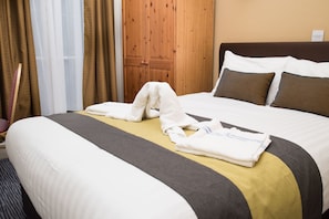A neatly made bed with a striped pillow, a folded towel, and a blanket. - Rose Court Hotel (London)