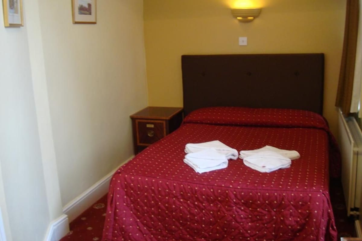 Una habitación de hotel con cama doble, mesita de noche y lámpara fijada a la pared.
