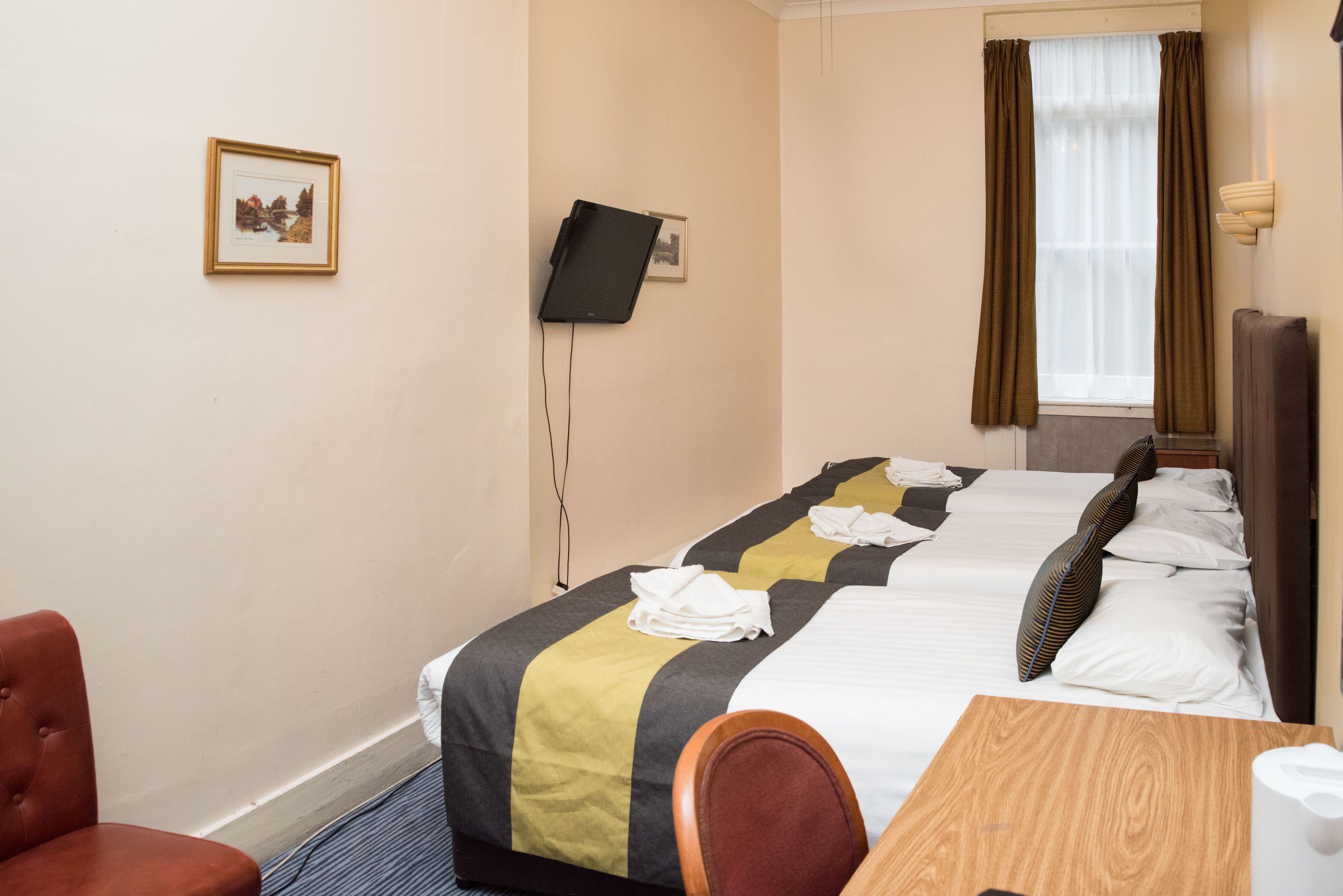 A hotel room with two beds, a desk, a chair, a television mounted on the wall, and a window with curtains.