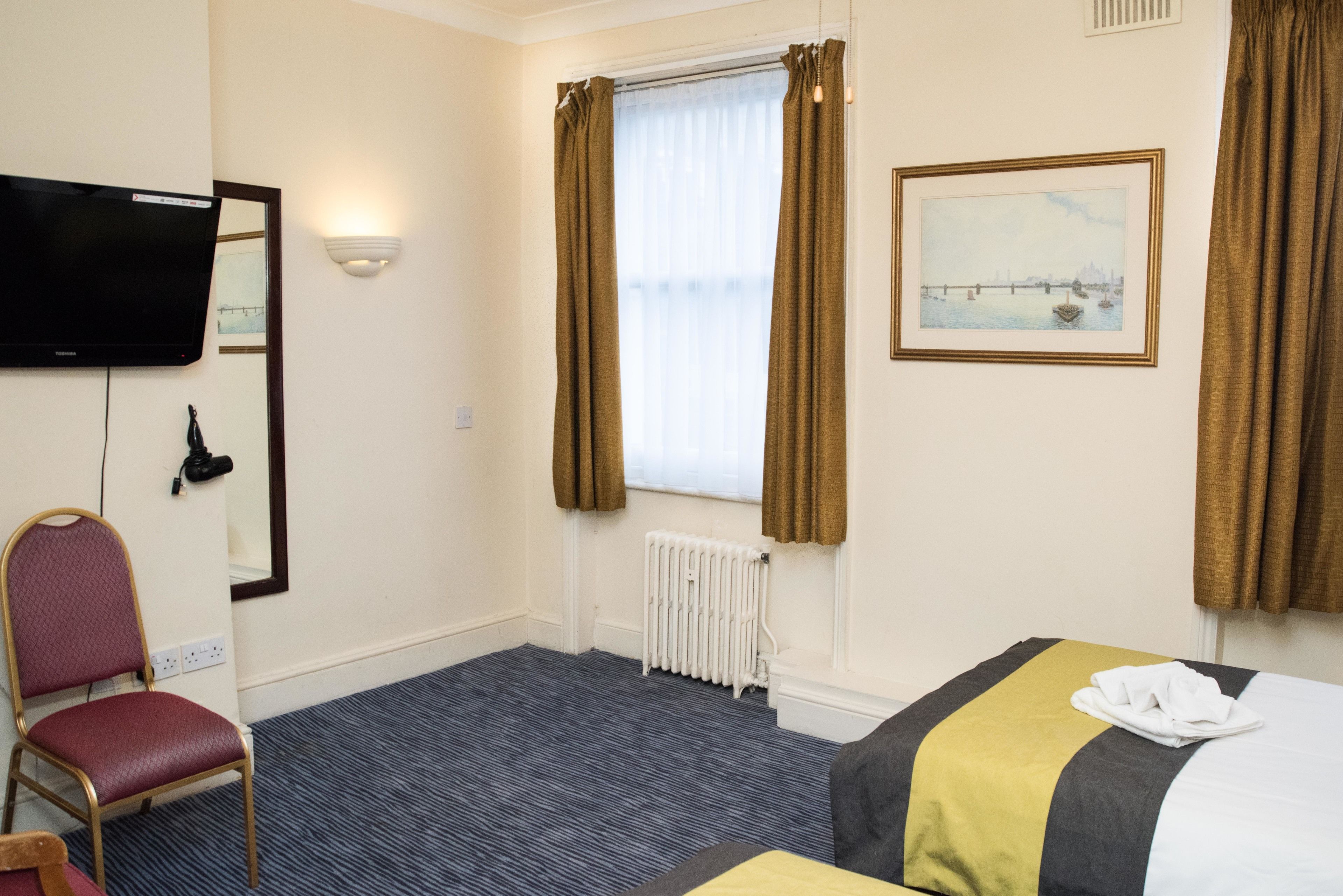 A hotel room with a bed, a chair, a television, a radiator, and a window with curtains.