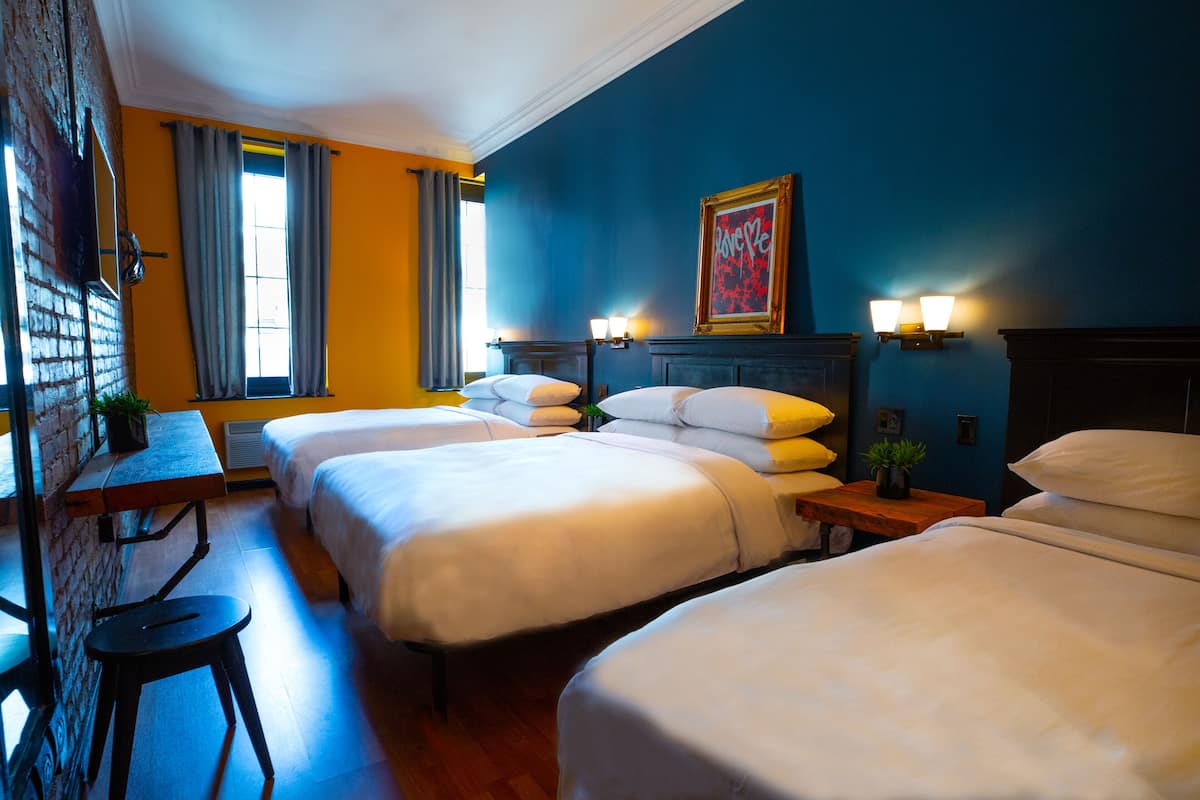 A hotel room with three beds, a desk, and a chair.
