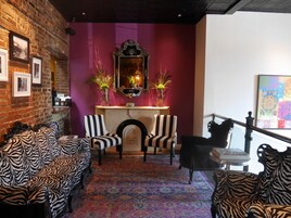 A room with a brick wall, a fireplace, striped chairs, and a zebra-patterned sofa.