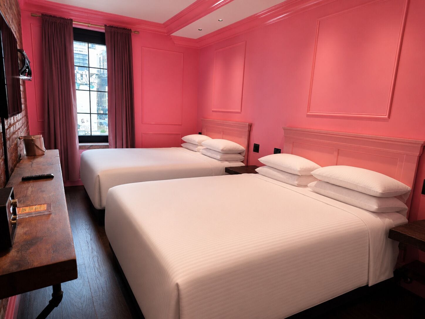 A hotel room with two beds, a wooden desk, and a window with curtains.