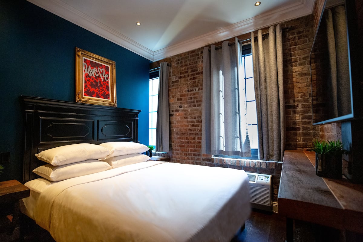 A hotel room with a large bed, a brick wall, and a window with curtains.