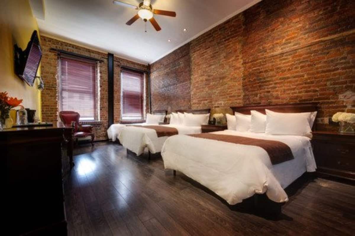 A hotel room with a brick wall, two beds, a desk, and a chair.