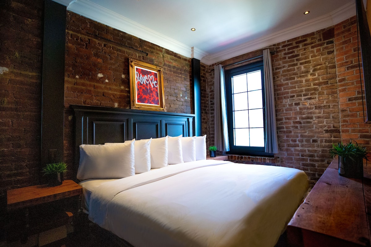 A hotel room with a large bed, a brick wall, and a window.