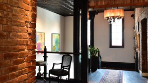 A room with exposed brick walls, a black chair, a table, a chandelier, and artwork on the wall.