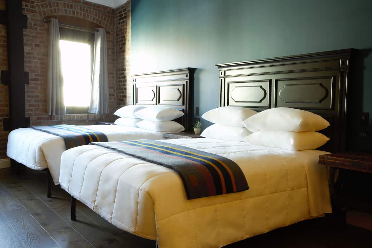 A double bed with a striped blanket, a nightstand, and a brick wall.