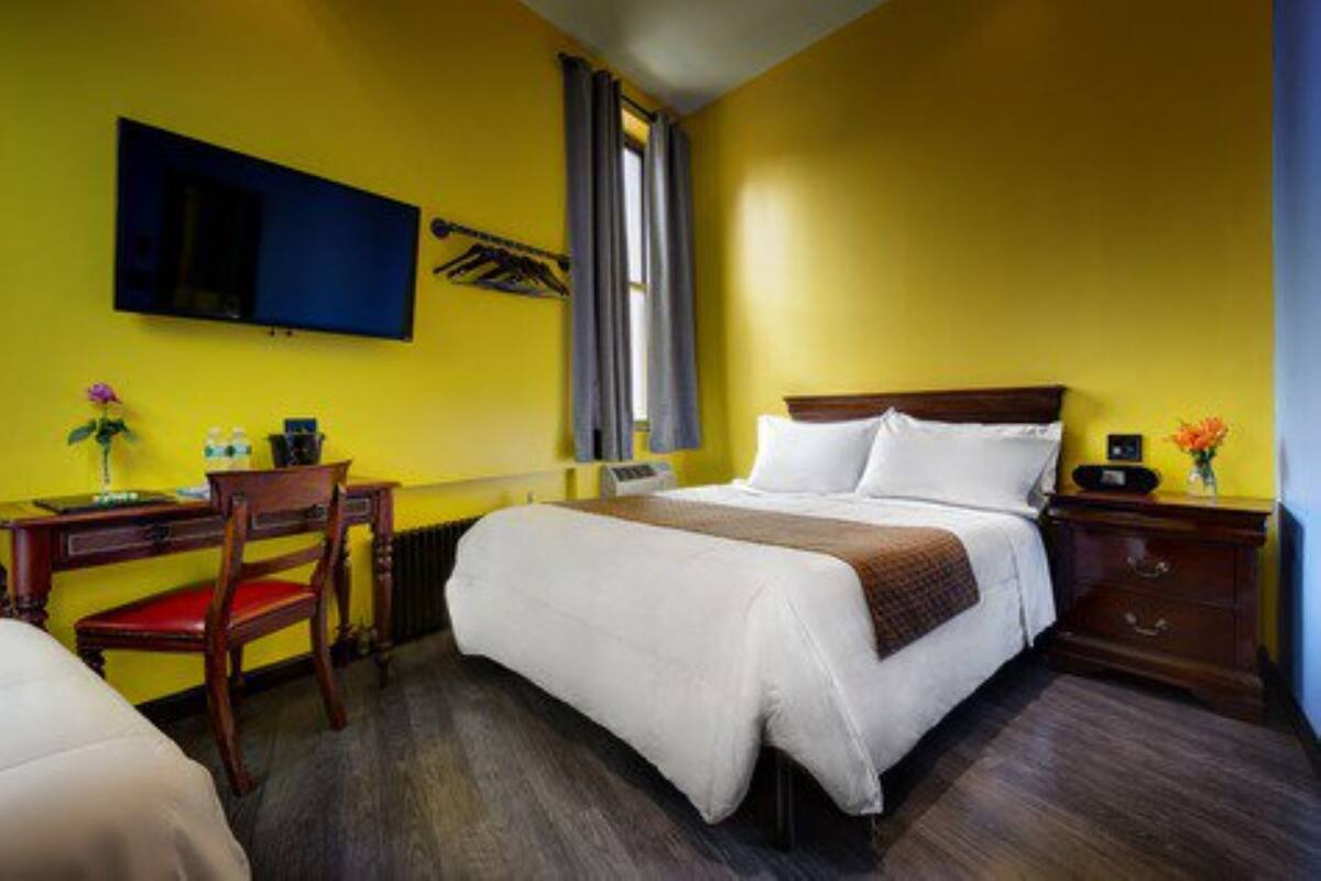 A hotel room with a bed, a desk, a chair, a TV, and a window with curtains.