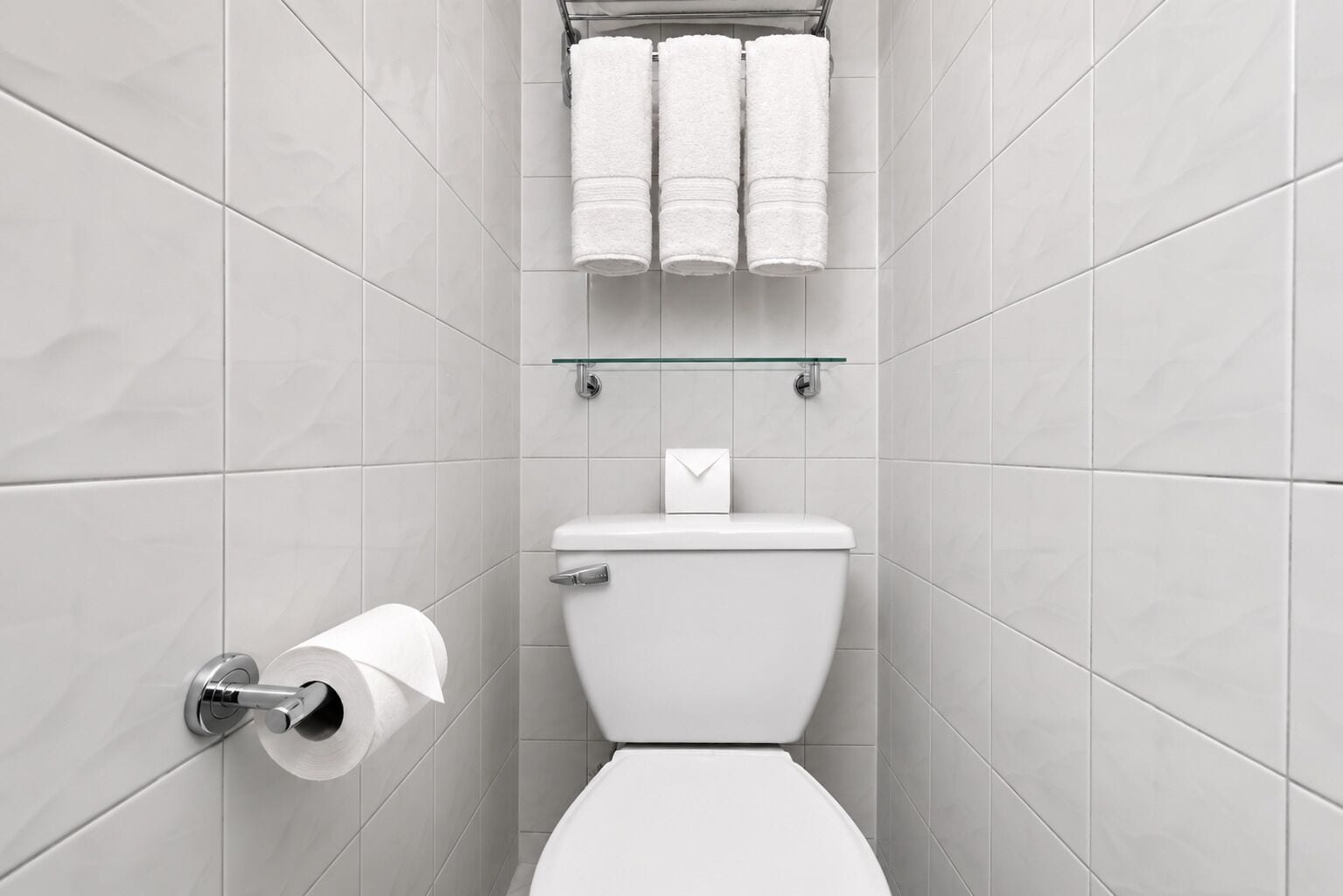 A modern bathroom with a toilet, a glass shelf holding towels, and a toilet paper holder.