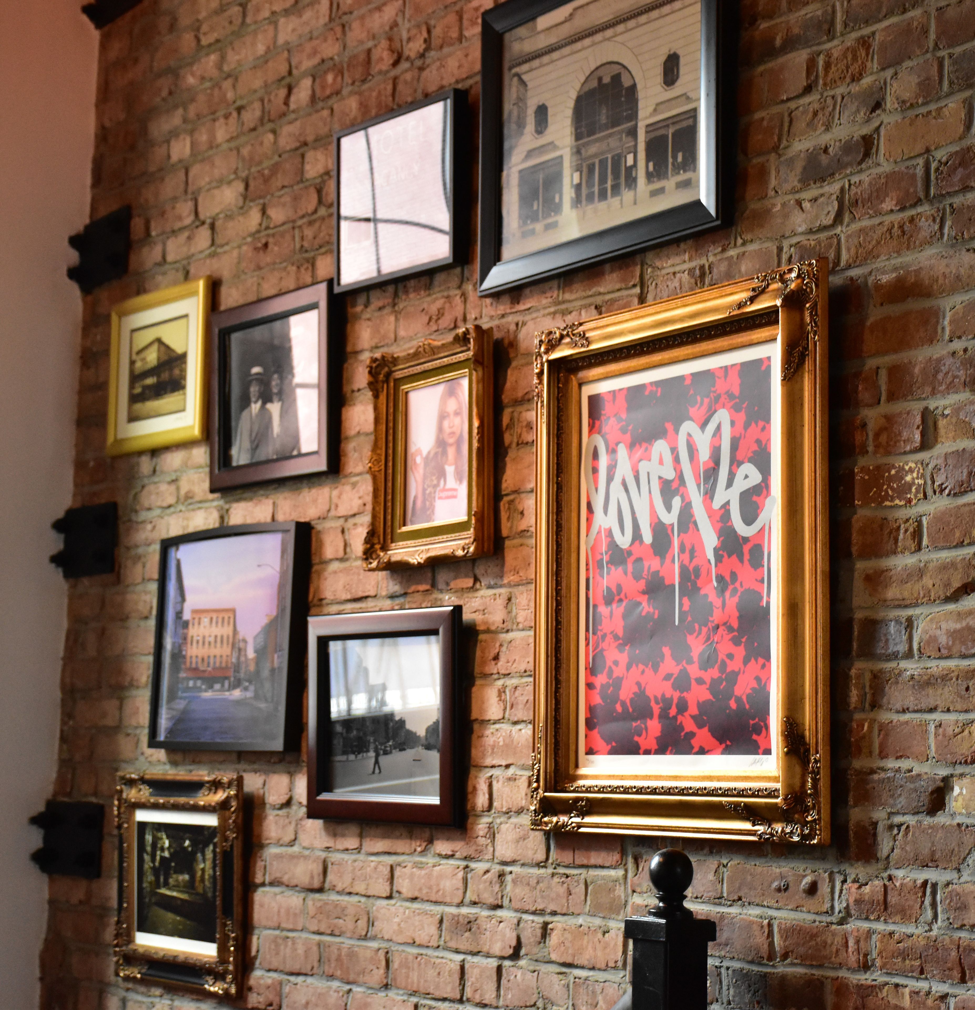 A wall with multiple framed pictures of buildings and a large framed poster with a red and black design.