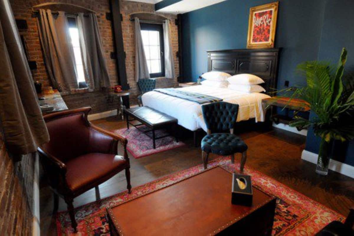 A hotel room with a large bed, a wooden desk, a leather armchair, and a potted plant.